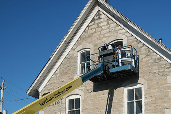 An outside look at installers installing a window on the second floor on a vintage home.