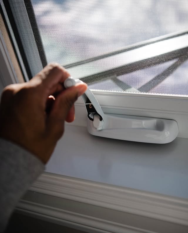 Close-up of a hand using a fold-down crank operator to open a casement window, showing how the operator mechanism controls the sash