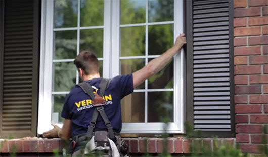 Un installateur de Verdun pose une fenêtre blanche à battant sur une maison en briques.